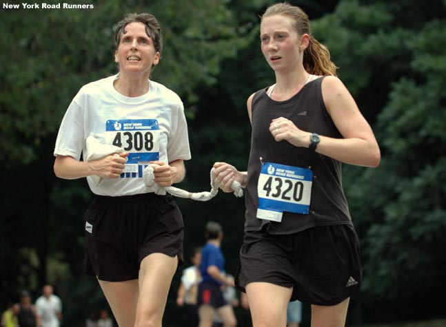 Clarissa Hitchon (right, 204th, 41:25) serves as a guide for Christa Earl (age 47, 205th, 41:25). Both represent the Achilles Track Club.